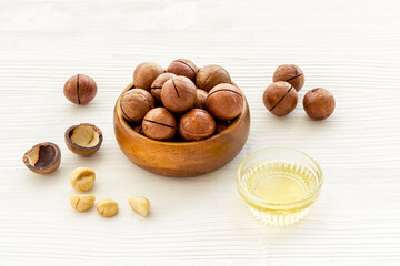Bowl of of macadamia nuts oil with raw nuts. Natural oil for cosmetic or cooking