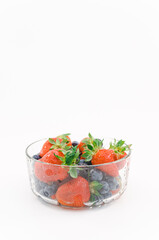 immagine primo piano di ciotola in vetro con frutti di bosco freschi da filiera biologica, fragole e mirtilli, superficie bianca	