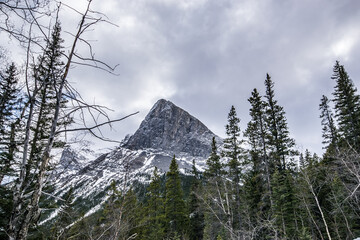Low angle view of a snow covered mountain peak against a cloudy blue sky. Cold day hiking through Grassi Lakes in Canmore, Alberta, Canada.