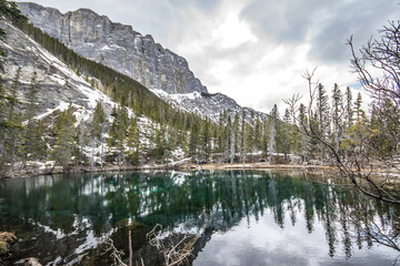 Looking out across the glacier lake at the amazing mountain views. It was a cold and icy hike up Grassi Lakes, in Canmore, Alberta, Canada.  - obrazy, fototapety, plakaty
