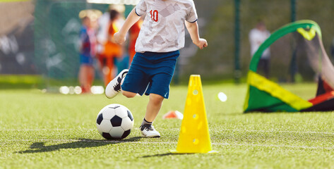 Little chlld running and kicking a soccer ball. Legs of young football player having fun during football match. European football youth player legs in action