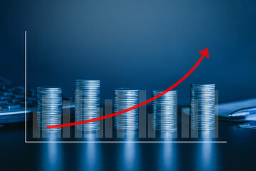 Stack of money coin on office desk with graph and red up curve arrow. Business and finance background concept with blue filter.