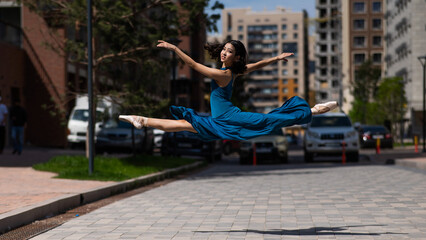 Fototapeta na wymiar Beautiful Asian ballerina dancing outdoors. Urban landscape. Grand jete. 