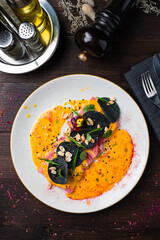 An appetizer of tuna, peanuts, black chips, sauce, sesame seeds and greens in plate.