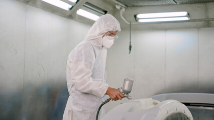 Car painters wear PPE over their heads and goggles over their mouths. standing in spray booth...