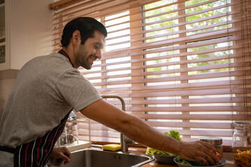 A handsome man washes vegetables in a kitchen for prepare a meal. Male at home with vegetables