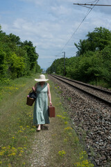 Portrait of woman walking on railways with a suitcase and summer hat