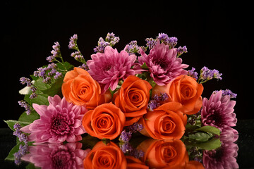 Beautiful orange roses surrounded by stunning floral arrangement in a studio setup on a reflective surface with light from behind. Inspirational as roses are the flower of love