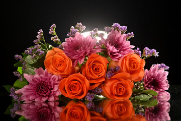 Beautiful orange roses surrounded by stunning floral arrangement in a studio setup on a reflective surface with light from behind. Inspirational as roses are the flower of love
