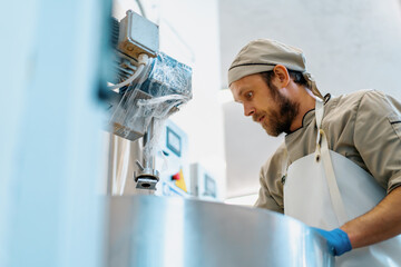 A worker mixing small pieces of a soft cheese in the vat with a big iron plate at the production in a cheese dairy