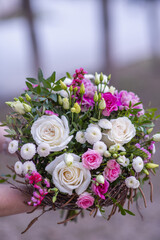A bouquet of white and pink flowers with greenery decorated in twigs in the hands