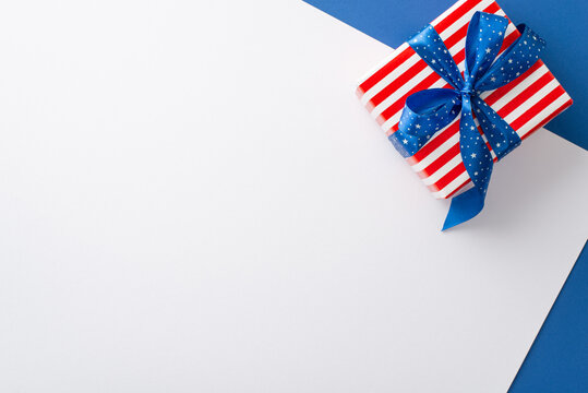 Patriotic setup for the Fourth of July. Overhead top view shot of party accessories, like big present box in national flag colors. White and blue backdrop with blank space for text or advertisement