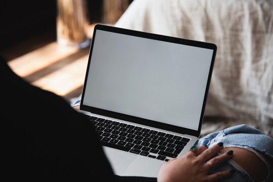 Woman Interacting with MacBook in a lap, browsing computer with blank screen mock-up for your design at home office with blurry background with free space for custom text about business
