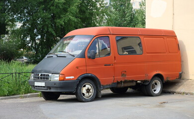 An old rusty red minibus is parked in the courtyard near the wall, Belysheva Street, St....