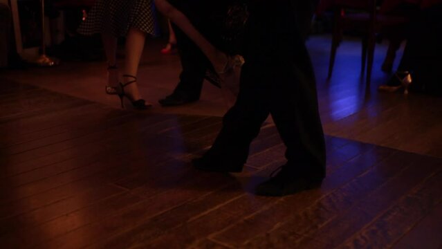 foot steps in the floor of a milonga dancing party, peopler dancing Argentine Tango in a moody bar cafe