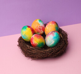 Easter colored eggs in nest on pastel color background. Easter still life