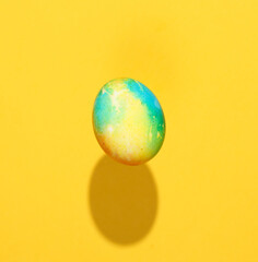 Multicolored Easter egg levitating on yellow background with a shadow