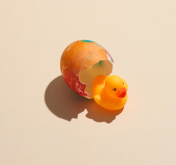 Hatched toy duck with a colored Easter egg on a beige background with shadow. Minimal easter concept