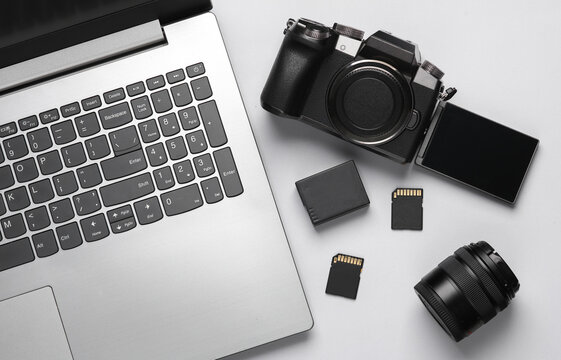 Laptop, Modern digital camera with flip screen, two sd memory cards, battery and lens on gray background. Photographer's equipment. Top view. Flat lay