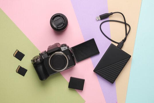Laptop, external hard drive, modern digital camera with flip screen, two sd memory cards, battery and lens on pastel background. Photographer's equipment. Top view. Flat lay