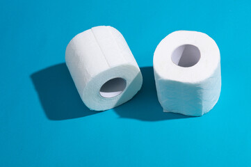 Two rolls of white toilet paper on a blue background with a shadow