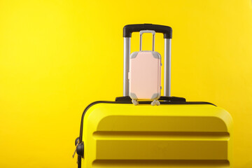 Yellow plastic travel suitcase and miniature on a yellow background. Luggage, tourism, vacation, relocation concept