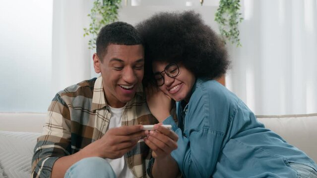 African American couple husband and wife happy girlfriend and boyfriend excited with positive pregnancy test replenishment in family happiness pregnant woman cuddling hugging with lovely man on couch