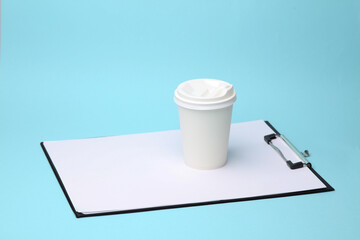 Conceptual business photo. Clipboard and white cardboard coffee cup on blue background. Creative layout. Template for design