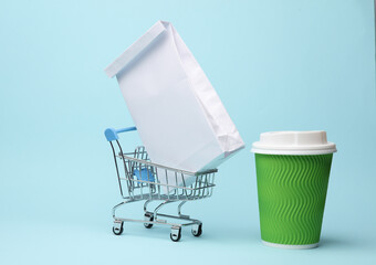 Paper lunch bag in supermarket troley with cardboard coffee cup on blue background