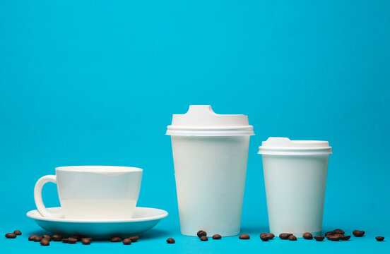 White cardboard and ceramic cups with coffee beans on a blue background. Template for design