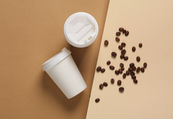 Disposable cardboard cups with coffee beans on brown beige background. Creative layout. Top view