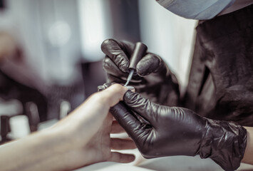 Manicurist paints with nail polish the nails of a woman's clint in nail salon. The working process