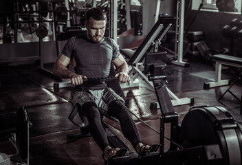 Male athlete trains strength and muscle endurance doing exercise in rowing machine in the gym