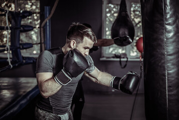 Fototapeta na wymiar Athlete boxer trains punches in boxing gloves with a punching bag