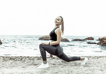 Fototapeta na wymiar Beautiful young fit woman in sportswear practicing stretching legs alone on wild beach. Healthy lifestyle concept