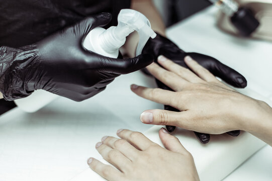 Manicurist workflow with model hands. Hands in black gloves sprays client's hands with liquid for manicure