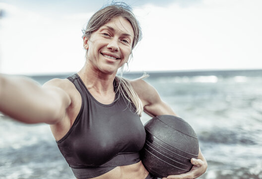 selfie portrait of Muscular woman athlete in sportswear with medicine balls on the beach