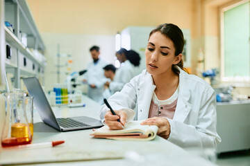 Female doctor takes notes while working on scientific research in laboratory.