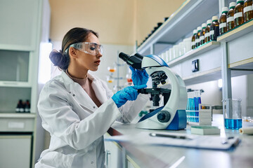 Naklejka na ściany i meble Female biochemist using microscope while working on scientific research in laboratory.