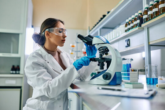 Female biochemist using microscope while working on scientific research in laboratory.