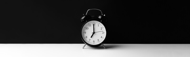 Black alarm clock on white table on black background.