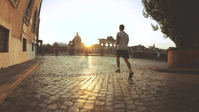 Young man in running clothes taking pictures in front of the Roman Forum at sunrise. Historical imperial Foro Romano in Rome, Italy from panoramic point of view.