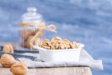 A close-up of walnuts on a blurry background. The walnuts are arranged in a white dish on a vintage rustic wooden table, and the background is soft and blurry.