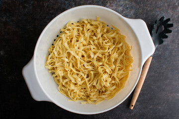 Cooked Tagliatelle Pasta in a Large Colander with a Pasta Spoon: Freshly cooked and drained noodles in a large strainer with a pasta fork