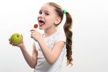 Fototapeta na wymiar A little girl licks a lollipop and holds an apple in her hand.