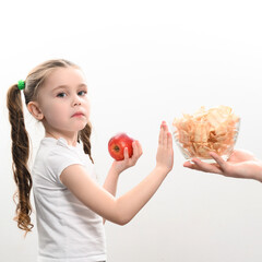 A big bowl of chips and apples, a beautiful little girl shows her displeasure with unhealthy food,...