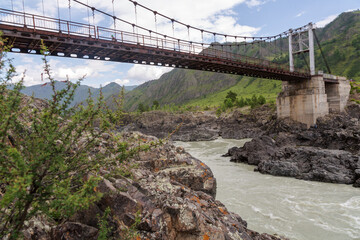 Oroktoysky Bridge - road suspension bridge over rocky banks of Katun River in green valley of Altai Mountains. Popular landmark in Chemal district of Altai Republic, Siberia, Russia