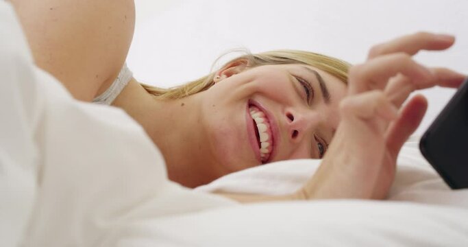 Woman, phone and happy for texting in bed with smile, excited face or reading chat on online dating website. Girl, smartphone and typing in bedroom, happiness and communication on social network app