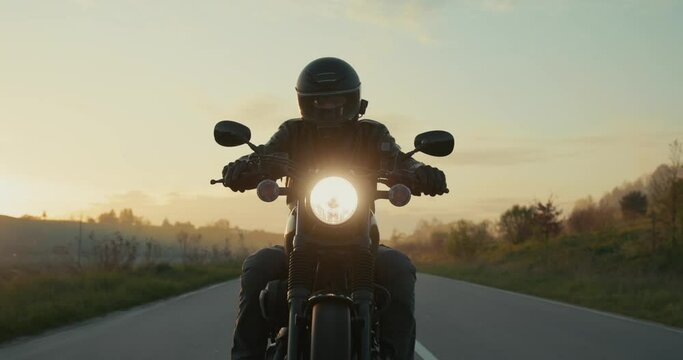 Slow-motion shot of a guy driving a black chopper motorcycle during a sunset.