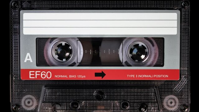 Audio cassette tape in use for sound recording in the tape recorder. A vintage, brand new blank red labelled music cassette playing back in a deck player. Static video camera shot. Close up, 4K
